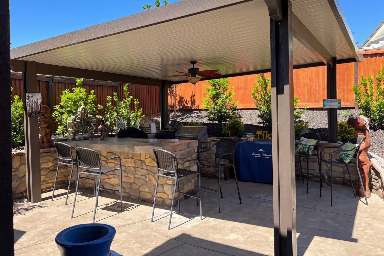 Bronze flat pan patio cover over a stacked-stone outdoor bar with bar stools and a built-in grill