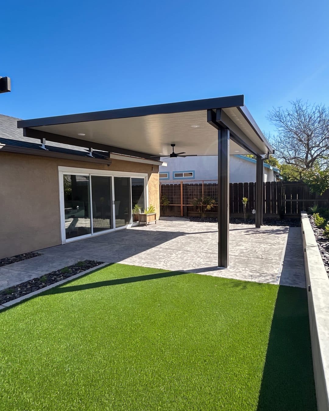 Bronze insulated patio cover with a smooth white ceiling over a stamped concrete patio and artificial lawn