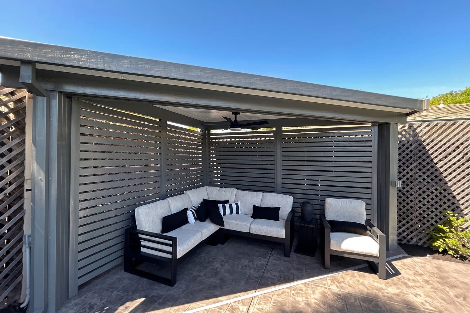 Gray insulated patio cover with slatted privacy walls sheltering a white outdoor sectional and lounge chair