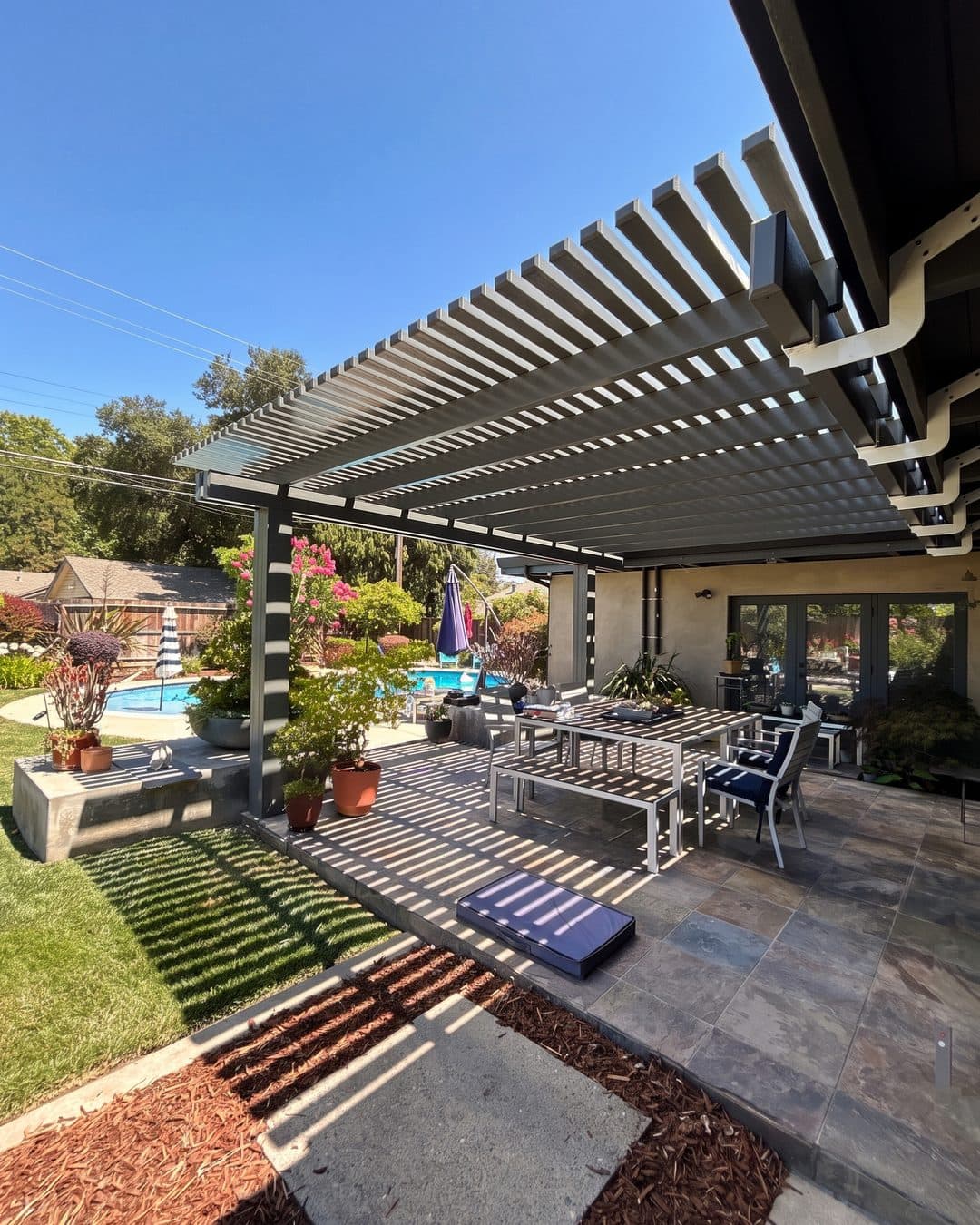 Gray lattice patio cover over a slate patio dining area beside a pool and flowering garden