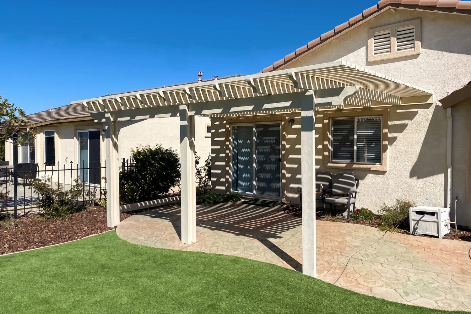 White lattice patio cover over a stamped concrete patio and curved lawn behind a tan home