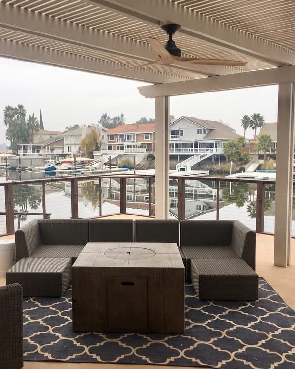 White lattice patio cover with a ceiling fan over a lounge set and fire table on a waterfront deck