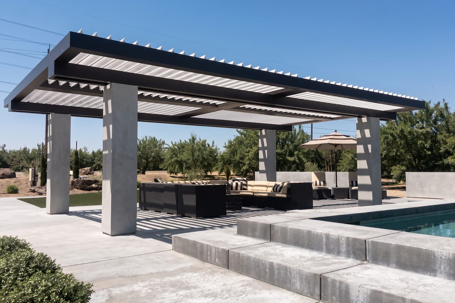 Modern freestanding louvered pergola with a black frame and concrete columns over an outdoor lounge beside a pool