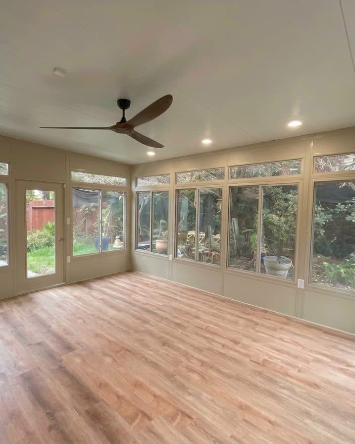Bright sunroom interior with recessed lights, a ceiling fan, wood-look floors and walls of windows facing the garden